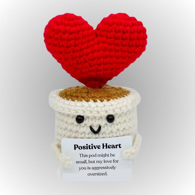 Crocheted heart-shaped pod with a smiling face and a tag on a light gray background. Positive heart succulent emotional support plush gift cute heart holding affirmative message gift for boyfriend girlfriend