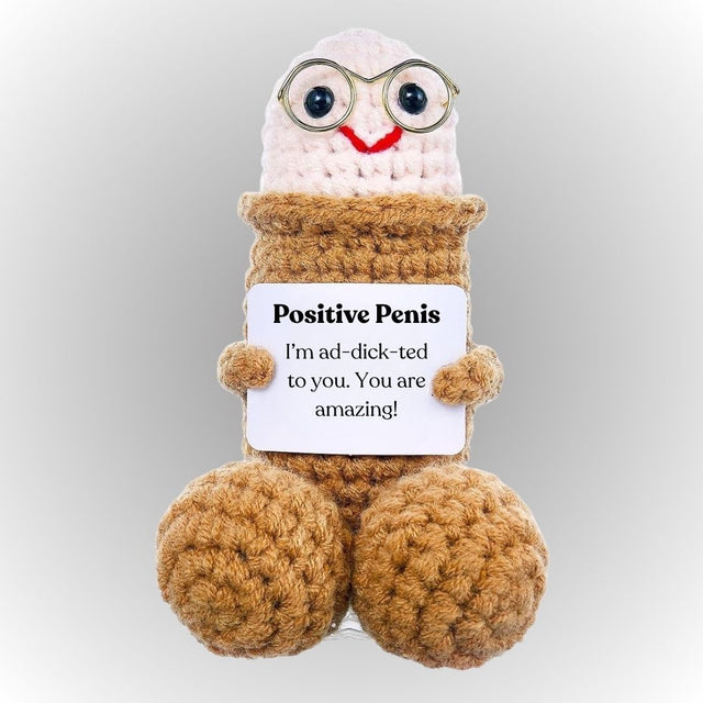 Plush toy resembling a penis with a sign reading 'Positive Penis' on a gray background. Positive dick emotional support plush cute small crochet weenie holding affirmative message gift for boyfriend girlfriend