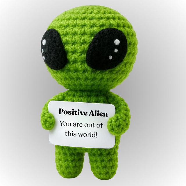 Green alien plush toy holding a sign with text on a white background. Positive alien emotional support plush space gift cute small green crochet alien UFO holding affirmative message gift for space lovers